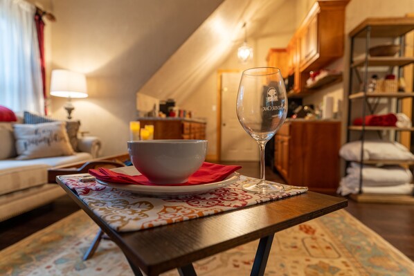 A cozy living room with a dining table set with a bowl and a wine glass, a sofa, and a lamp.