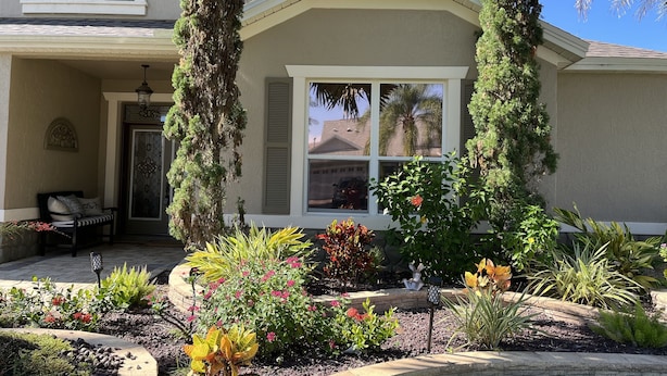 Ein Haus mit überdachter Veranda, einem Fenster mit Fensterläden und einem Garten mit verschiedenen Pflanzen und Blumen.