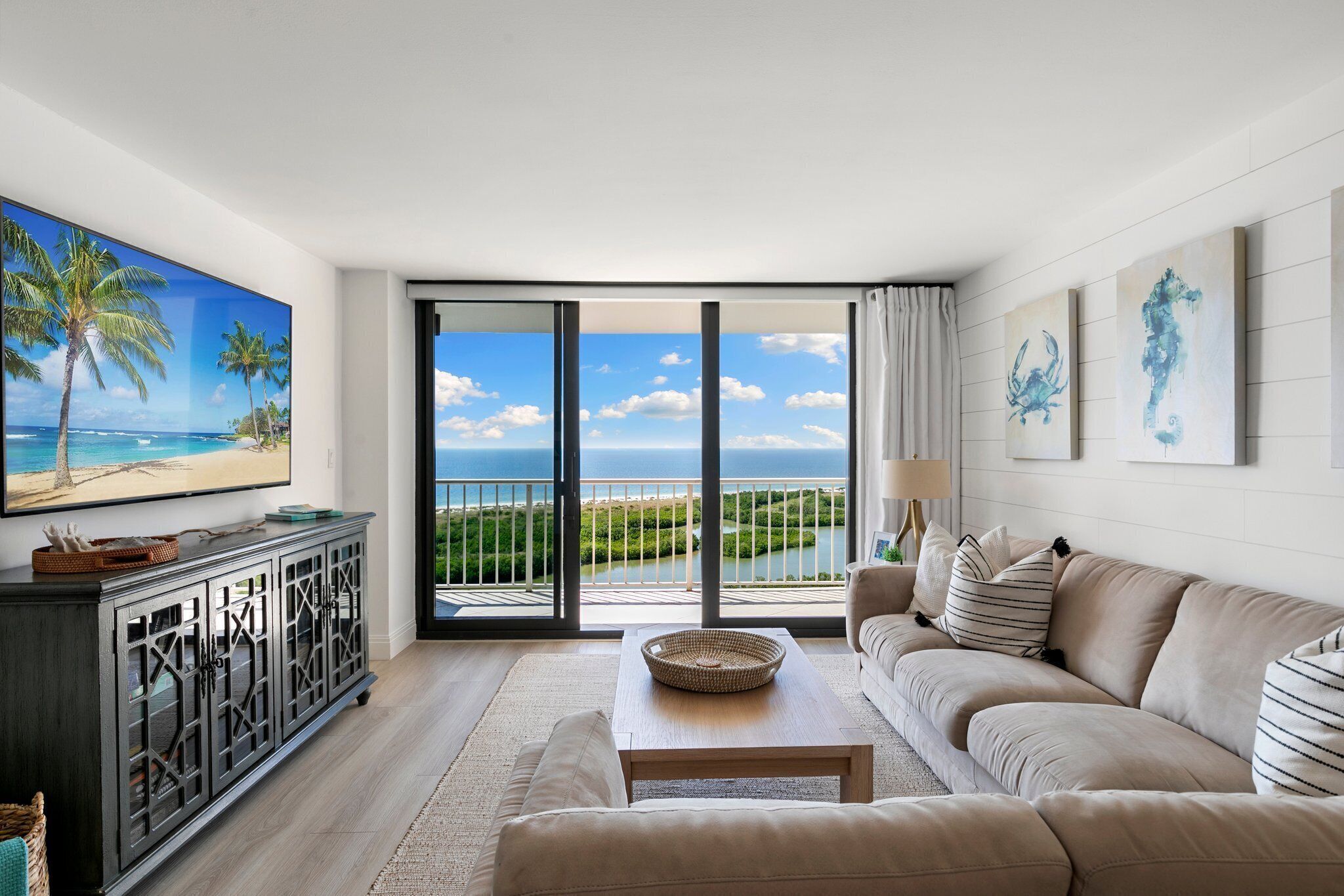 Un salón moderno con un ventanal grande con vista a la playa, un televisor de pantalla plana, un sofá y una mesa de centro.
