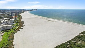Paesaggio costiero con un'ampia spiaggia sabbiosa, edifici alti e un cielo azzurro e limpido.