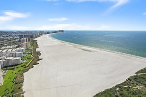 Een kuststadsgezicht met een breed zandstrand, hoge wolkenkrabbers en een helderblauwe lucht.