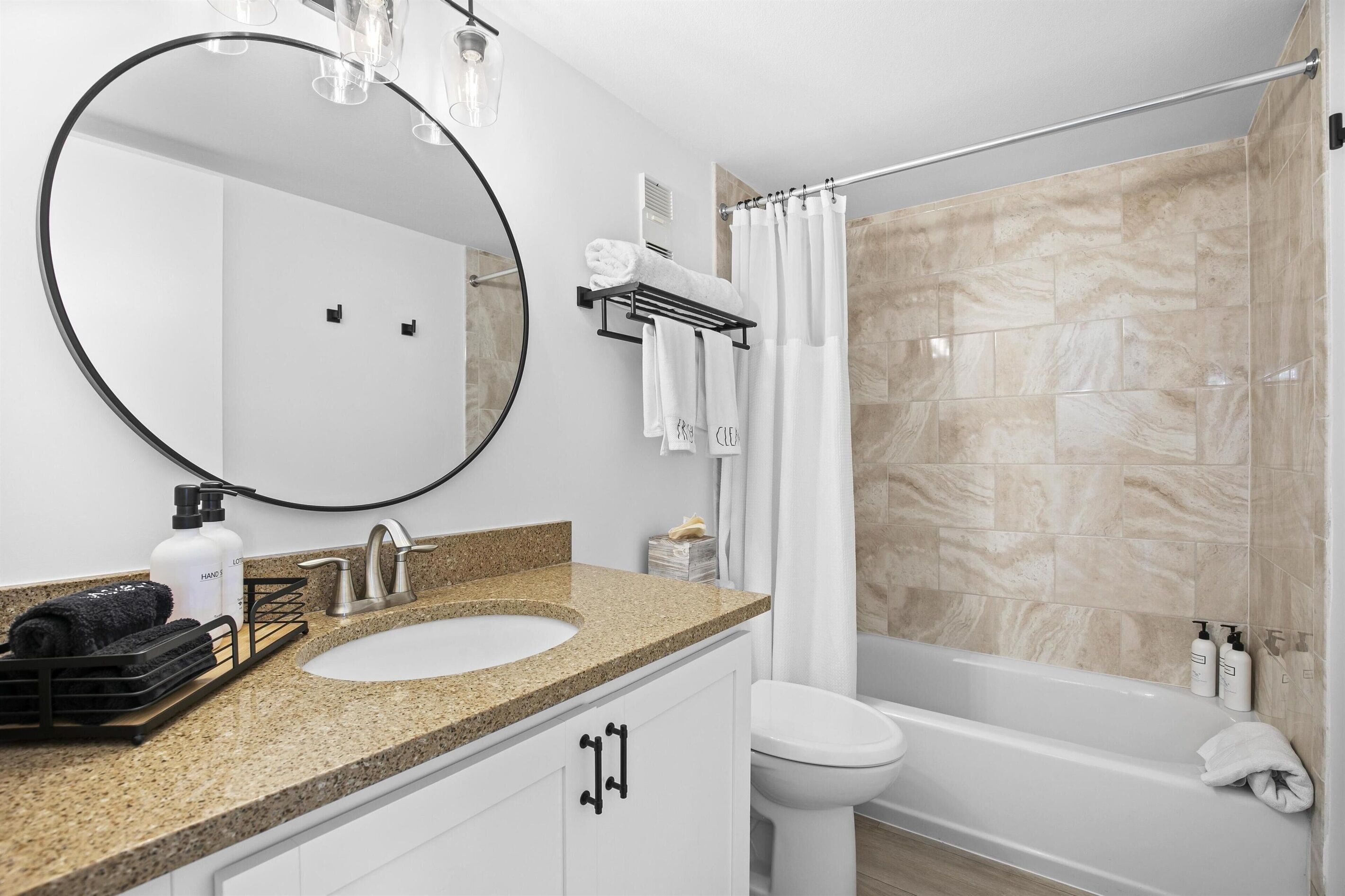 Un bagno moderno con uno specchio rotondo, un lavandino, un water e una vasca da bagno.
