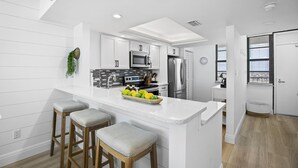 Una cucina moderna con mobili bianchi, un'isola centrale con sgabelli, un forno a microonde e un frigorifero.