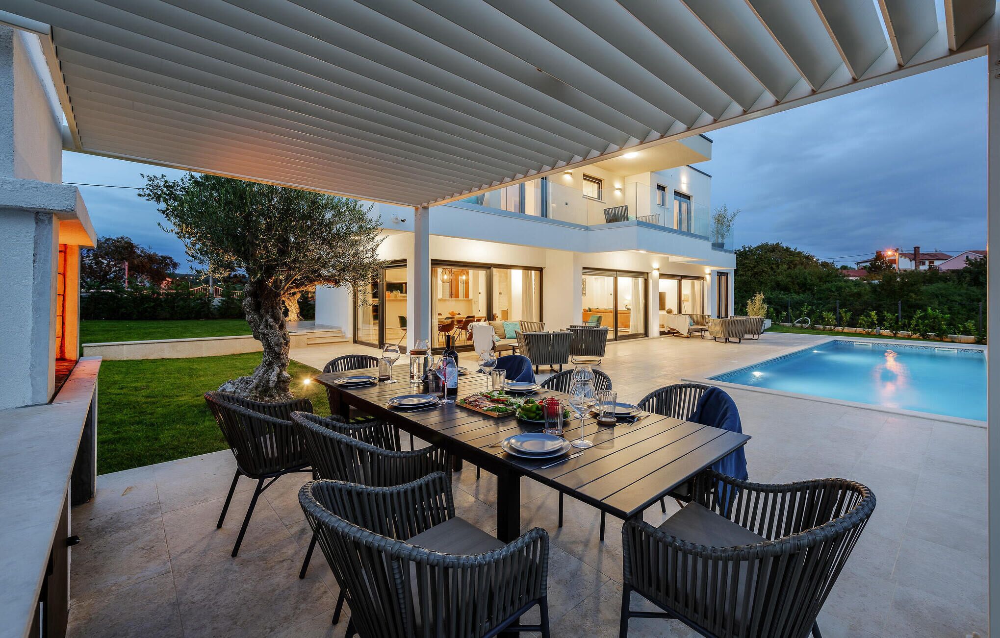 Een buitenterras met zwembad, overdekte patio en een modern huis op de achtergrond.