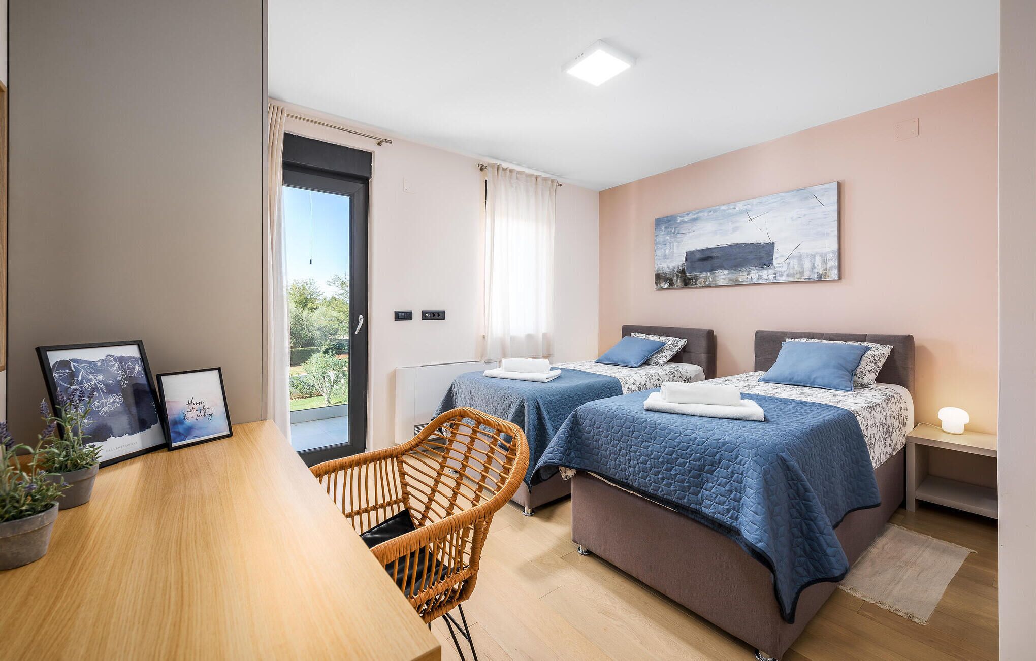 Ein modernes Schlafzimmer mit zwei Betten, einem Holztisch, einem Korbstuhl und einem großen Fenster.