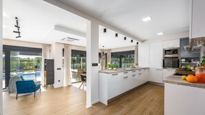 Een moderne keuken met witte kasten, een houten vloer en uitzicht op een zwembad.