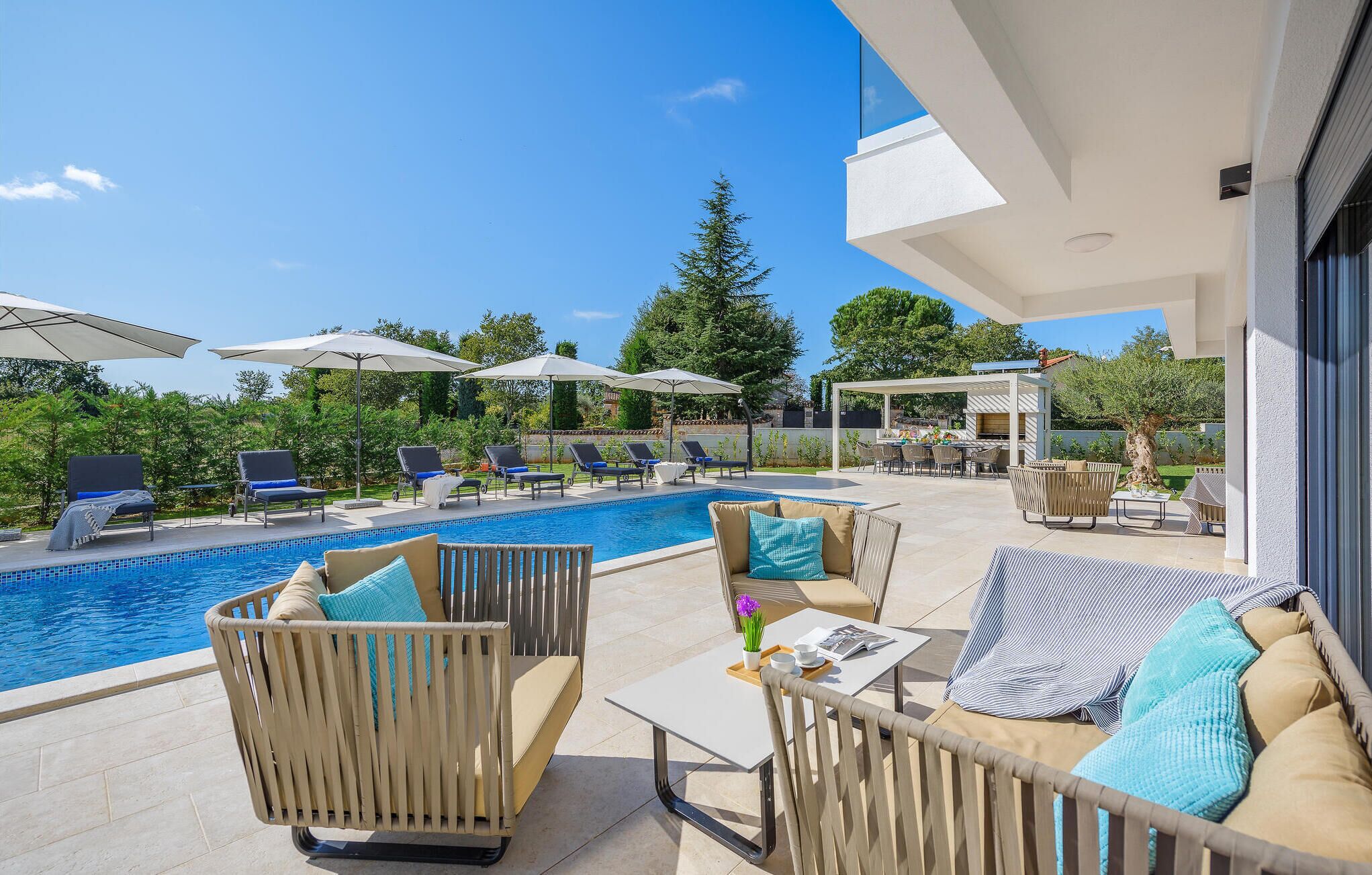 A poolside area with lounge chairs, umbrellas, and a barbecue setup.