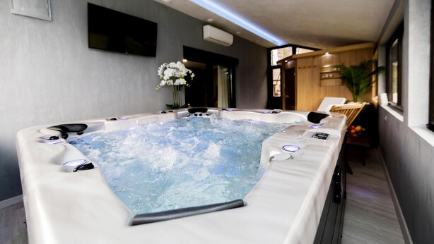 Un grand bain à remous rectangulaire doté de plusieurs jets, d’un panneau de commande et d’un espace détente avec des fauteuils.