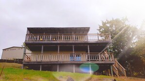 A two-story wooden building with balconies, a staircase, and a grassy area with rocks. - Eufaula Lakefront House In Quiet Neighborhood w/ Private Dock & Game room (Canadian)