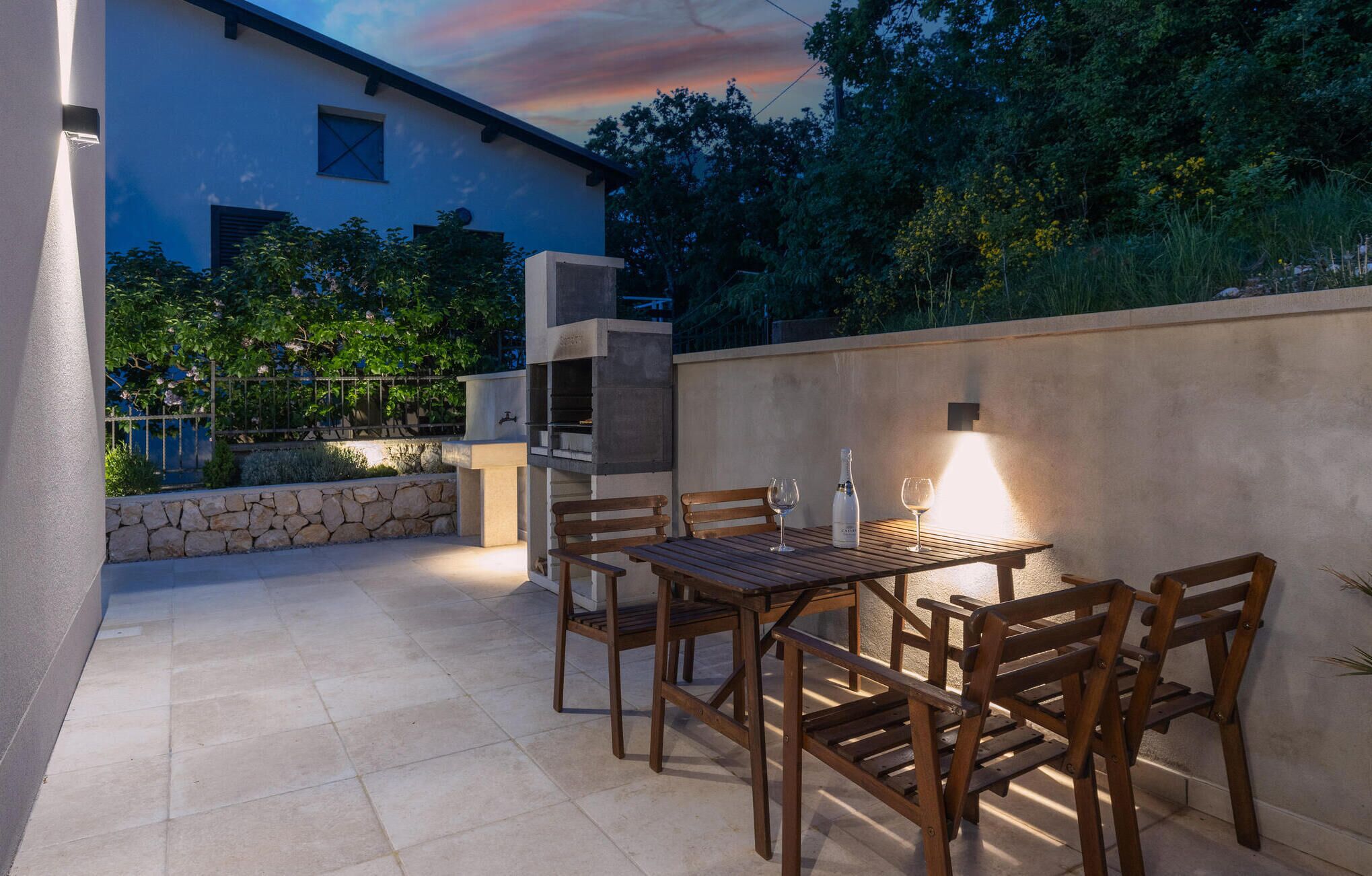An outdoor patio with a table and chairs, a grill, and a wall-mounted light.