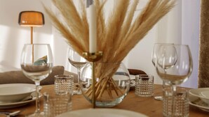 Une table à manger dressée avec des assiettes, des verres et un vase contenant des herbes des pampas séchées.