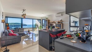 Espaço de estar moderno com uma janela ampla que oferece uma vista panorâmica, área de cozinha com balcão e um espaço para sentar com sofá e mesa de centro.