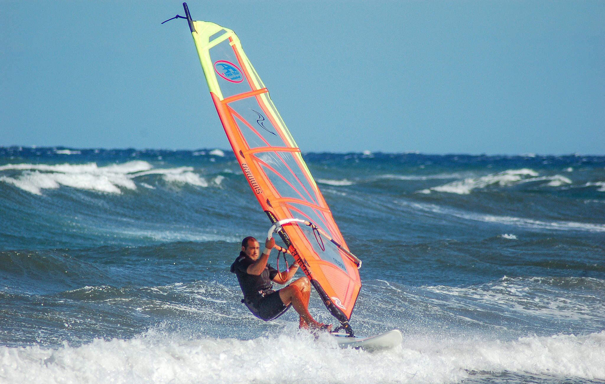 A person windsurfing on a surfboard with a colorful sail.