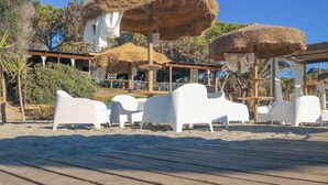 Um resort à beira-mar com guarda-sóis de palha, espreguiçadeiras brancas e um deck de madeira.