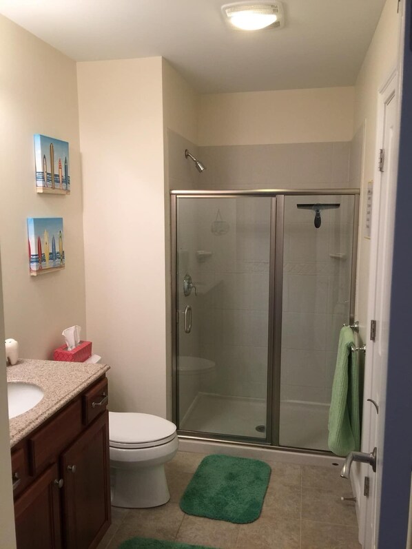 A bathroom with a glass-enclosed shower, a toilet, a sink, and a cabinet. - Oceanfront Penthouse Condo with Beautiful Beach View (Hampton)