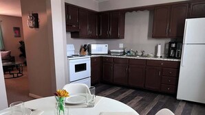 A modern kitchen with dark brown cabinets, a white refrigerator, and a dining area with a round table set for two. - Apt 3 Comfortable and Convenient (Masury)