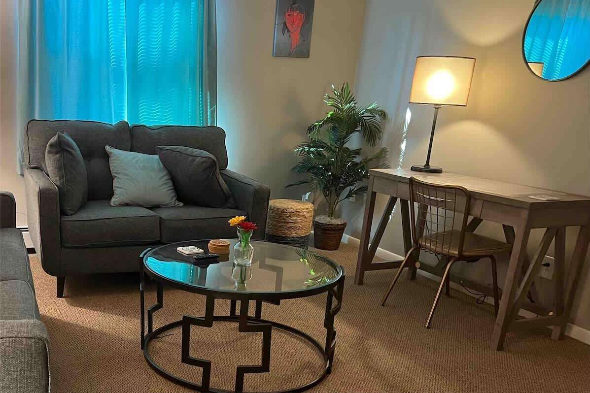 Ein Wohnzimmer mit einer Couch, einem Glastisch, einer Lampe, einem kleinen Tisch und einer Topfpflanze.
