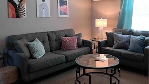 A living room with two grey sofas, a glass coffee table, and a lamp. - Apt 3 Comfortable and Convenient (Masury)