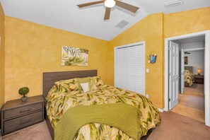 A bedroom with a bed, a nightstand, a ceiling fan, a door, and a wall-mounted picture.