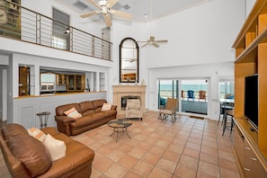 A spacious living area with a fireplace, a sofa set, a television, and a balcony with outdoor seating.