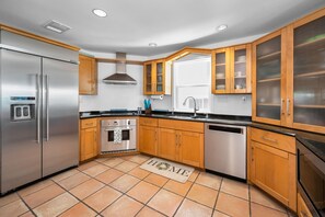 A modern kitchen with stainless steel appliances, wooden cabinets, and a tiled floor.