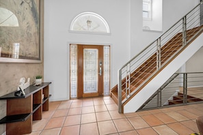 A modern interior with a staircase, a glass door with a geometric pattern, and a tiled floor.
