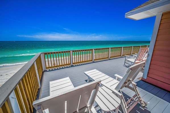 A deck with white chairs overlooking a beach with clear turquoise water.