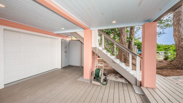 Eine überdachte Terrasse mit Holzboden, eine weiße Garagentür und eine Treppe mit weißer Geländer.