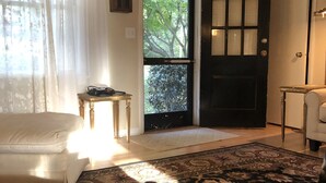 A living room with a white sofa, a laptop on a striped ottoman, a patterned rug, and a door leading outside.