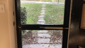 A view through a door screen, displaying a grassy area with a pathway and a house in the background.