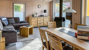 A cozy living room with a sofa, a wooden coffee table, a dining table with chairs, a cabinet, and a large window. - Nice home in Rechlin with sauna (Rechlin)