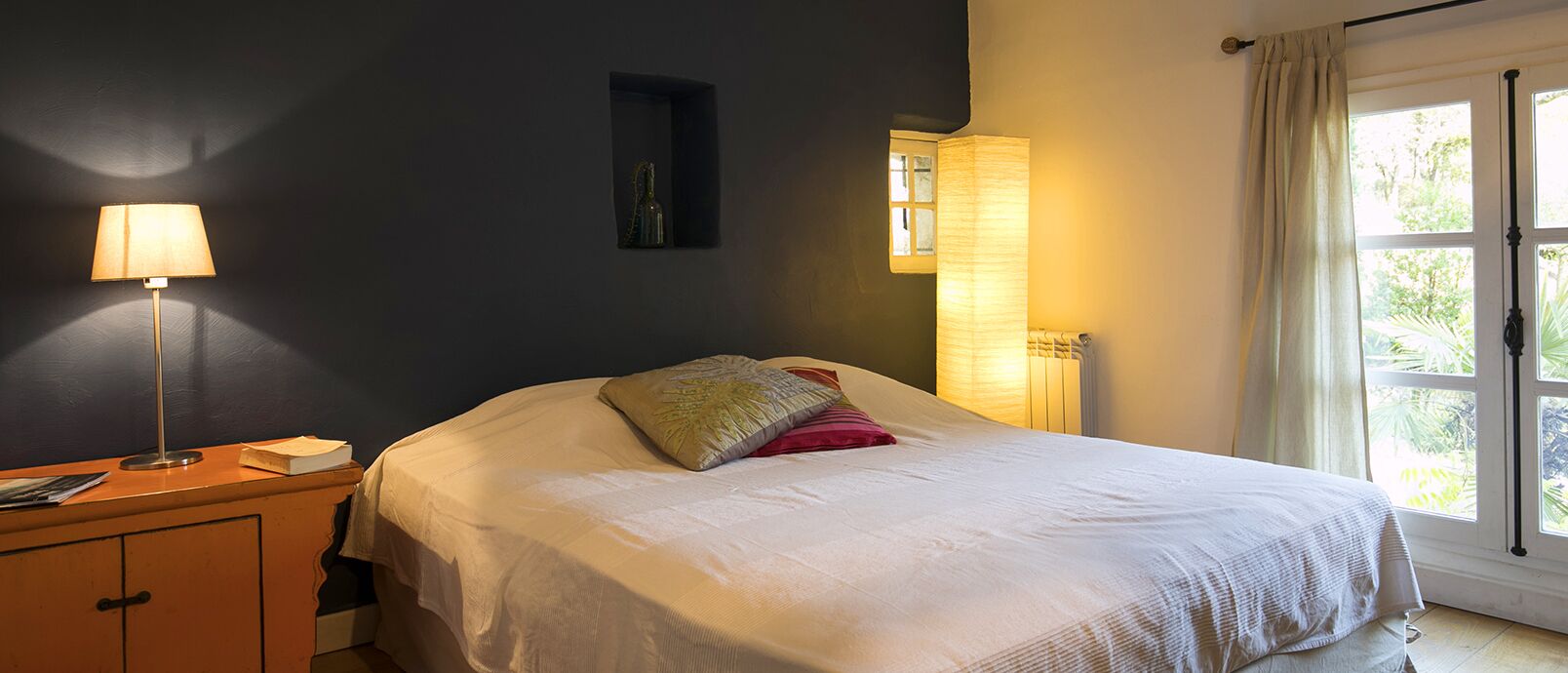 Une chambre à coucher avec un lit, une table de chevet, une lampe et une fenêtre.