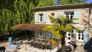 A stone building with a covered patio, outdoor seating, and a palm tree. - Magnificent restored farmhouse in Crillon-le-Brave with swimming pool  (CRILLON LE BRAVE)
