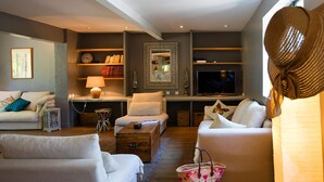 A modern living room with a sofa, armchairs, a coffee table, and a television. There are shelves with books and decorative items, and a large mirror on the wall. - Magnificent restored farmhouse in Crillon-le-Brave with swimming pool  (CRILLON LE BRAVE)