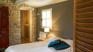 A bedroom with a stone wall, a wooden door, a window with a lamp, and a bed with blue pillows. - Magnificent restored farmhouse in Crillon-le-Brave with swimming pool  (CRILLON LE BRAVE)