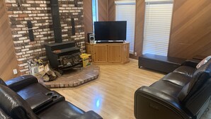 Uma sala de estar com lareira de tijolos, sofás de couro, uma televisão de tela plana e armários de madeira.