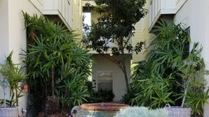 A courtyard with potted plants and flowers, a central fountain, and a building with a balcony in the background. - Beautiful Condo!!  Boutique Complex,  Private Beach Access,  Pool (Santa Rosa Beach)
