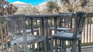 A wooden deck with a table and chairs, overlooking a coastal landscape with palm trees and a building in the background. - Beautiful Condo!!  Boutique Complex,  Private Beach Access,  Pool (Santa Rosa Beach)