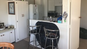 Uma cozinha compacta com armários brancos, geladeira, micro-ondas e um pequeno espaço de jantar com dois banquinhos.