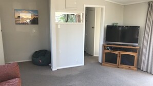 Sala de estar com televisão de tela plana em suporte de madeira, um bean bag e porta que dá para outro cômodo.