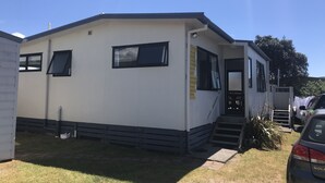 Uma casa móvel térrea com varanda frontal, uma garagem pequena acoplada e um cano de água visível.
