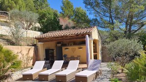 Un área de estar al aire libre techada con sillones de mimbre y una mesa, rodeada por una terraza de madera y vegetación natural.