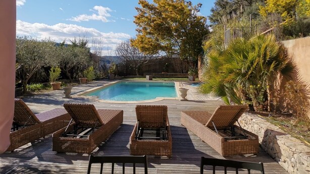 Un área junto a la piscina con sillones de mimbre y una piscina azul cristalina.