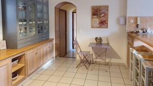 Una cocina con un armario de madera, una lámpara colgante, una mesita con una silla y un cuadro en la pared.