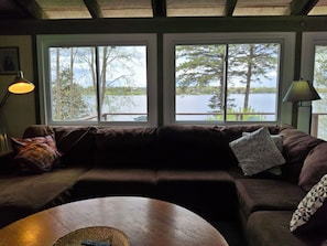 A living room with a brown sofa, two windows overlooking a lake, and a lamp on the right. -  Gone Fishing!  Is Pet Friendly! (South Hero)