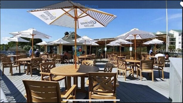 An outdoor seating area with round tables and chairs, umbrellas, and a wooden deck. - Hilton Head First Floor Ocean View with Balcony, Pool, and Tennis (Hilton Head Island)