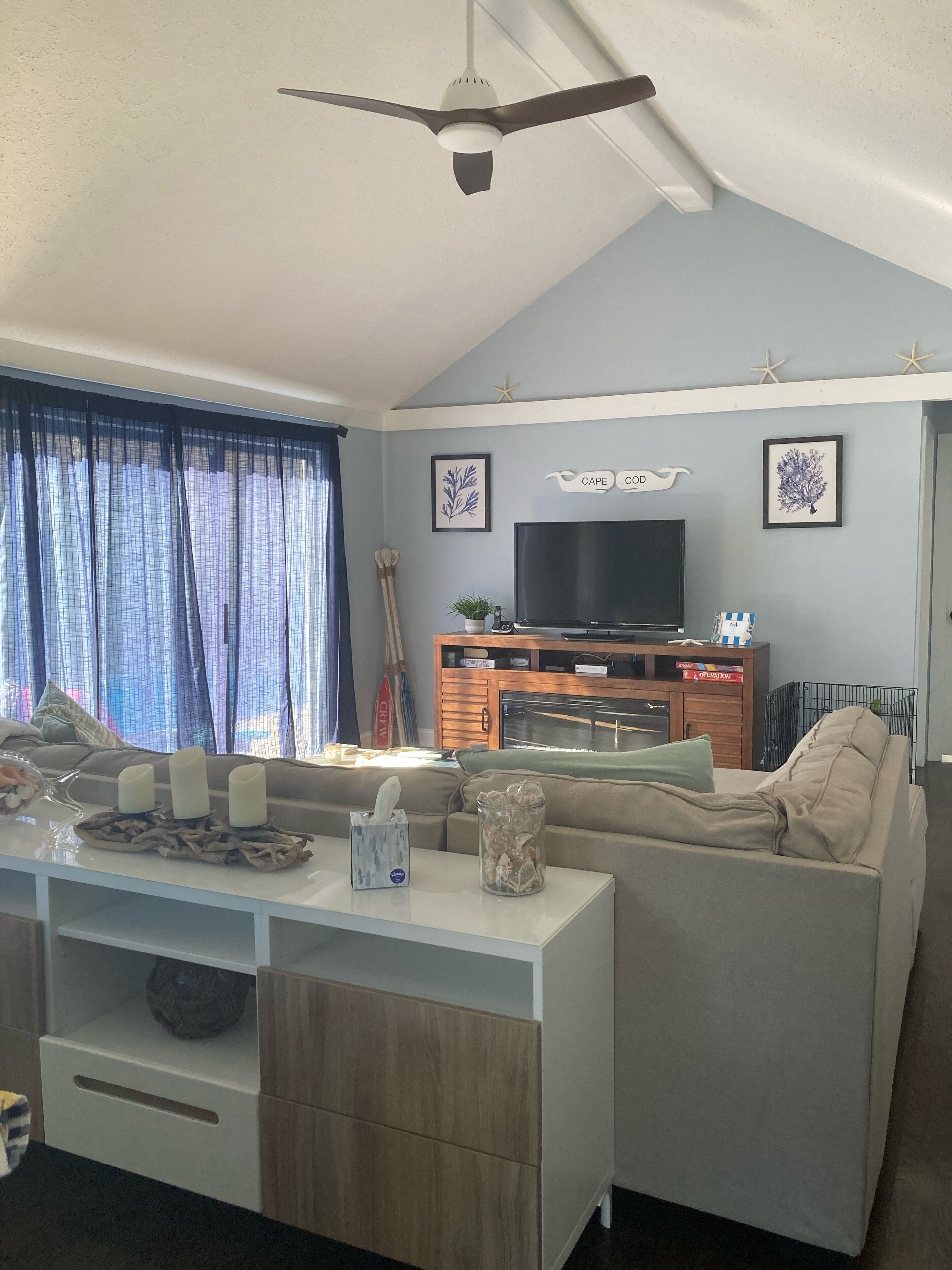 A living room with a ceiling fan, a flat-screen TV, a wooden cabinet, and a sofa.