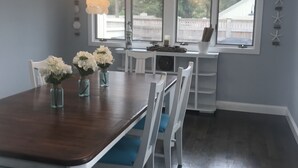 En matplats med ett träbord och vita stolar, en kristallkrona och utsikt genom stora fönster.