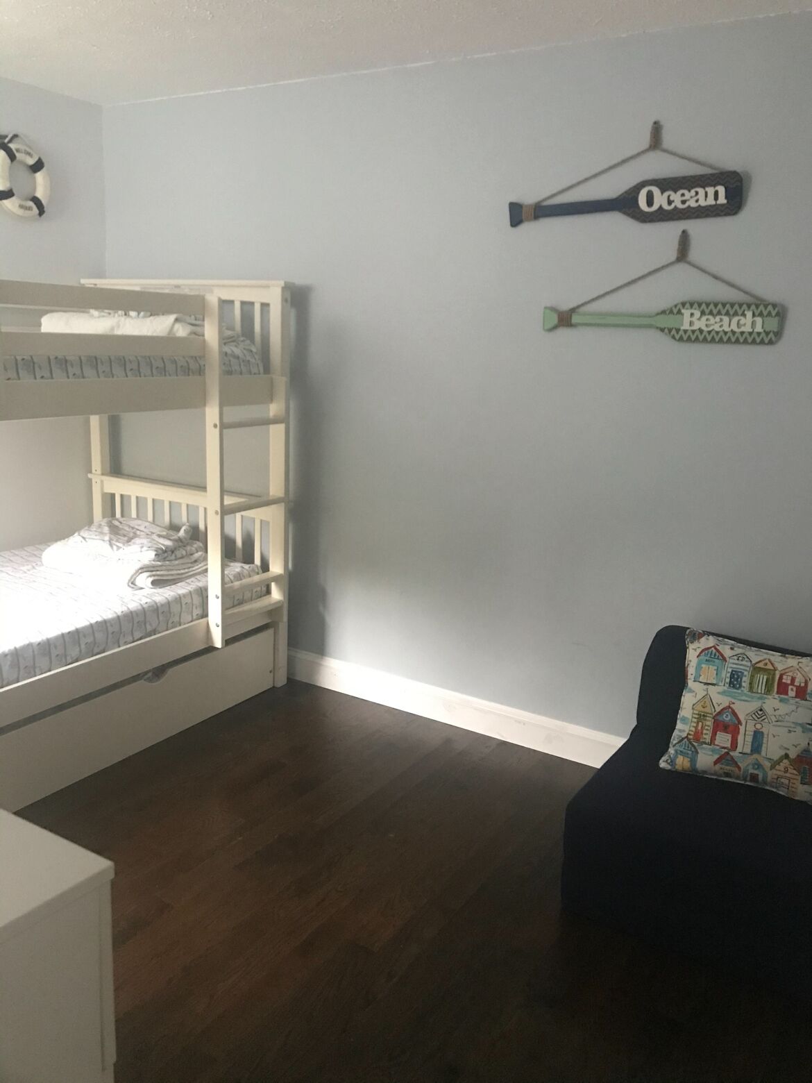 Una habitación con una cama litera, un pequeño sofá y una pared donde cuelgan un bozal de salvamento y un bate.