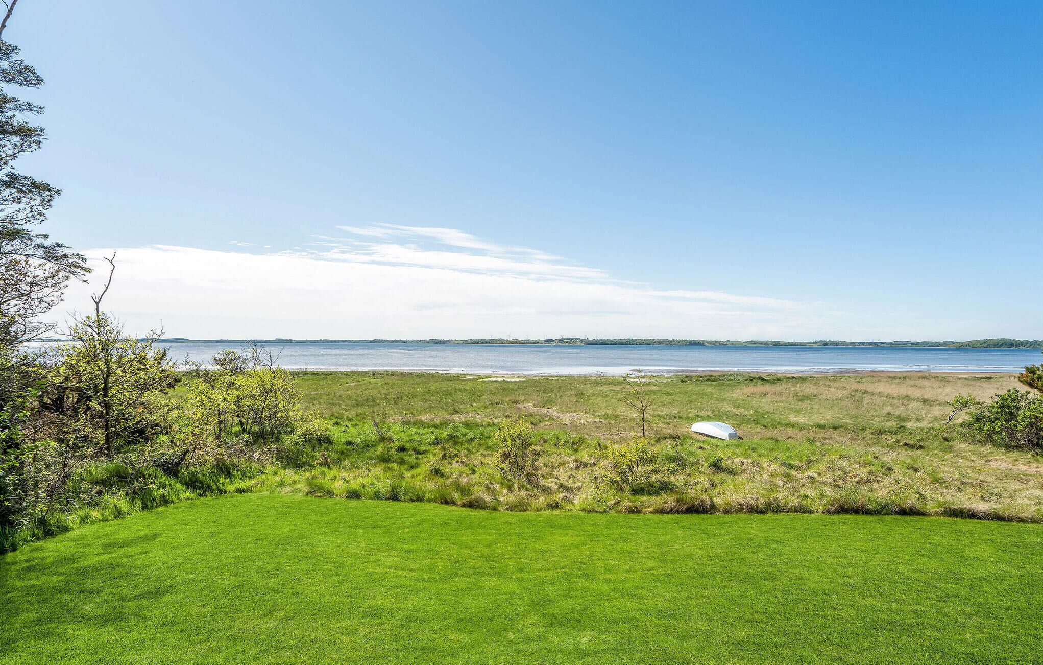 A grassy field with a boat on the shore, a clear sky, and a distant shoreline.